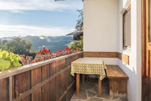Ein Balkon mit einer Holzbank und einem Tisch, einer weißen Wand und Blick auf die Berge.