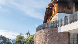 Una casa moderna con parete in pietra, balcone in legno e vista sul paesaggio circostante.
