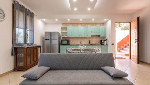 Una sala moderna con un sofá, un aparador de madera y una cocina al fondo.