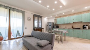 Una cocina moderna con armarios color turquesa, una mesa de comedor y un sofá gris en una sala de estar luminosa.