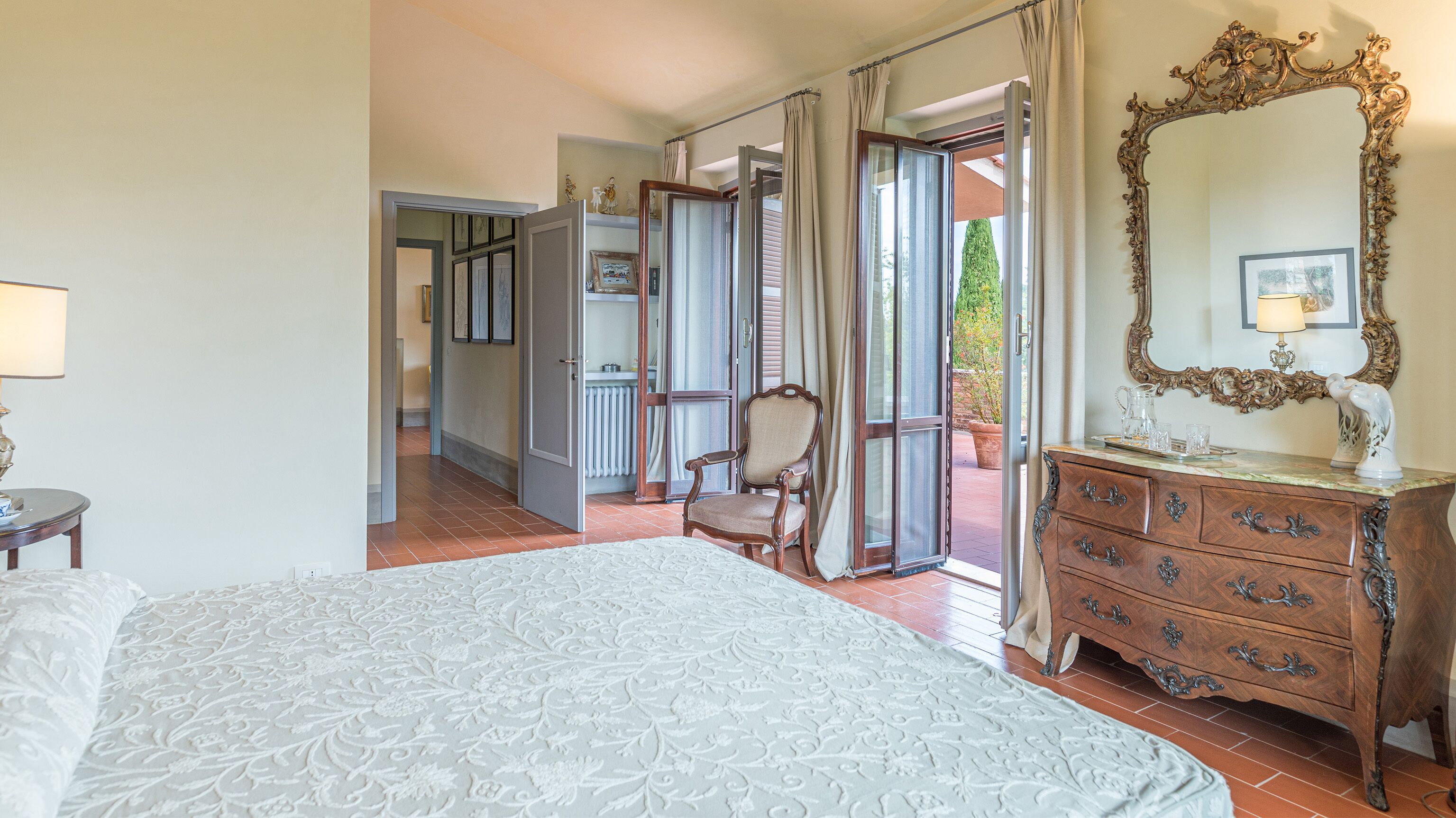 A bedroom with a large bed, a dresser with drawers, a chair, and a mirror.