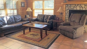Una sala de estar acogedora con sofás de cuero, una chimenea de piedra y un ventanal.