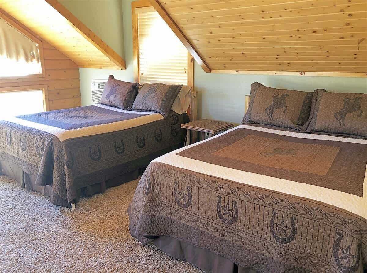 Two beds with patterned bedding in a room with wooden beams and a sloped ceiling.