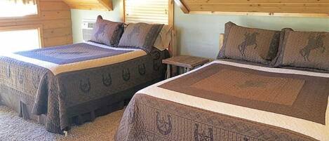 Two beds with patterned bedding in a room with wooden beams and a sloped ceiling.