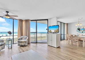 Relax in a spacious living area with a sofa, armchairs, and dining table, leading to a balcony with a beach view.