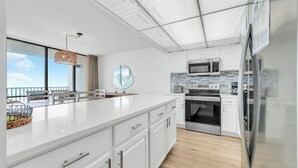 Cozinha moderna com armários brancos, eletrodomésticos de aço inoxidável e uma grande janela com vista para uma varanda.
