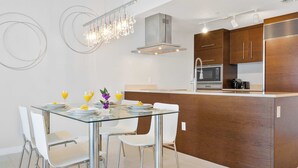 A modern kitchen with a glass dining table, white chairs, and stainless steel appliances.
