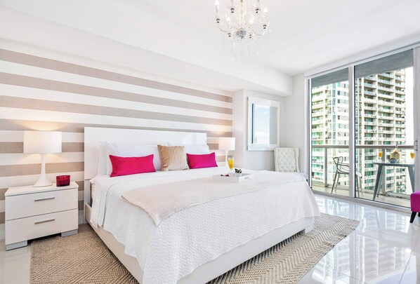 A modern bedroom with a large bed, striped walls, a chandelier, and a balcony with a city view.