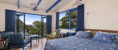 Une chambre avec un grand lit, une tête de lit en bois et une vue sur l’extérieur. Elle comprend un balcon avec des chaises et une table.