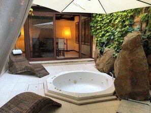 Ein Whirlpool in einem sonnendurchfluteten Außenbereich mit Korbmöbeln, einer Glastür, die zu einem Raum führt, und einer mit Efeu bewachsenen Wand.
