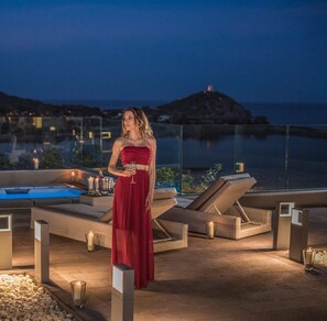 A woman in a red dress standing on a rooftop terrace with lounge chairs, candles, and a pool. - Beautiful Luxury Villa Located in Sardinia in Villasimius Near the Beaches (Villasimius)