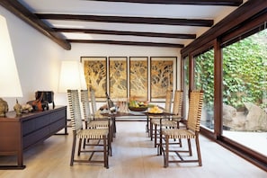 A dining area with a wooden table and chairs, a decorative lamp, and a large window with a view of greenery. - Beautiful Luxury Villa Located in Sardinia in Villasimius Near the Beaches (Villasimius)