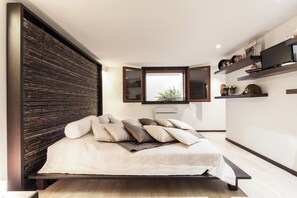 Ein modernes Schlafzimmer mit Bett, Fenster, einer Kommode mit Dekoration und einem Fernseher.