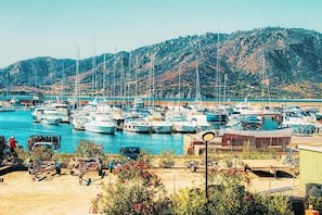 A marina with boats docked, a mountainous backdrop, and a small building in the foreground. - Beautiful Luxury Villa Located in Sardinia in Villasimius Near the Beaches (Villasimius)