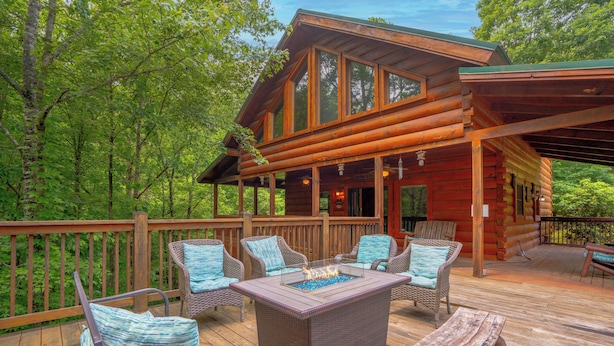 A log cabin with a deck featuring wicker furniture and a central fire pit. - Majestic Splendor Lodge: Spacious deck, Home Theater, Game Room, Wooded View, near Attractions! (Sevierville)