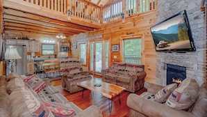 A spacious log cabin interior with a living room, kitchen, and dining area. - Majestic Splendor Lodge: Spacious deck, Home Theater, Game Room, Wooded View, near Attractions! (Sevierville)