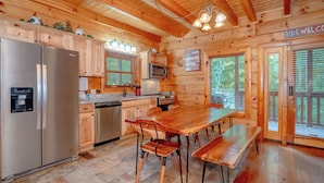 A wooden cabin-style kitchen with a refrigerator, microwave, and wooden cabinets. - Majestic Splendor Lodge: Spacious deck, Home Theater, Game Room, Wooded View, near Attractions! (Sevierville)
