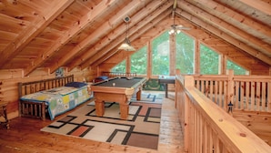 An attic room with a pool table, a billiards table, and a large window. - Majestic Splendor Lodge: Spacious deck, Home Theater, Game Room, Wooded View, near Attractions! (Sevierville)