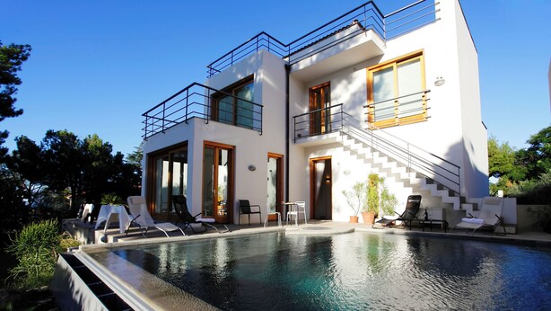 Una casa moderna de dos pisos con piscina, mobiliario exterior y una escalera que conduce al nivel superior.