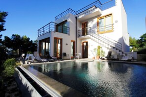 Ein modernes, zweigeschossiges Haus mit Swimmingpool, Sitzgelegenheiten im Freien und einer Treppe, die zu der oberen Etage führt.