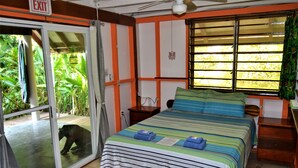 A room with a bed, a window with blinds, a door with an exit sign, and a view of greenery outside. - Jungle Like Oasis in San Ignacio - Secluded Cabaña Retreat Close To Mayan Ruins (San Ignacio)