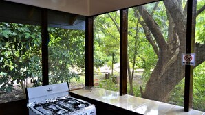 A gas stove in a kitchen with a view of a lush garden through large windows. - Jungle Like Oasis in San Ignacio - Secluded Cabaña Retreat Close To Mayan Ruins (San Ignacio)