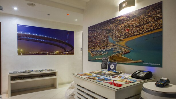 A reception desk with a large poster of a coastal cityscape, a phone, and a payment terminal. - Room-bella Pescara B&b - Abruzzo, Italy (Pescara)