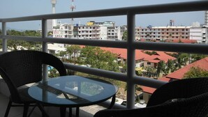 Un balcone con un tavolo in vetro e sedie in vimini, con vista su un paesaggio urbano caratterizzato da edifici e una torre.