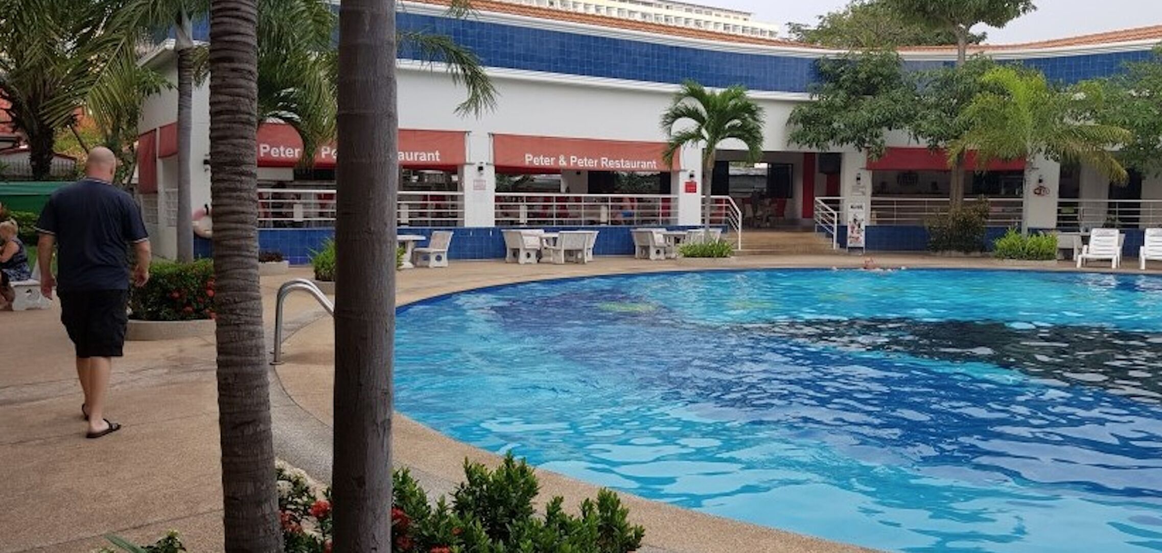 A swimming pool with lounge chairs and a restaurant named "Peter & Peter Restaurant" in the background.