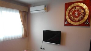 A bedroom with a bed, a wall-mounted TV, an air conditioner, and a decorative wall piece. - Park Lane Condo F4 R419 (Pattaya)