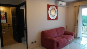 A modern living room with a red sofa, a glass coffee table, and a wall-mounted artwork. - Park Lane Condo F4 R419 (Pattaya)