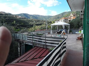 Eine Terrasse mit Blick auf eine Berglandschaft, einem überdachten Sitzbereich und einem kleinen Tisch mit Topfpflanzen.