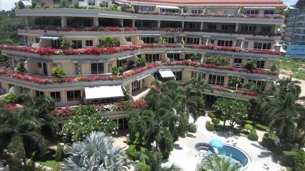 Een hotel met meerdere verdiepingen, met bloembalkons, een centraal gelegen zwembad en weelderige beplanting.