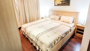 Een net opgemaakt bed met een bedspreide en kussens, een houten hoofdbord en een nachtkastje met een lamp.