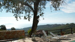 Una terrazza con tavolo e sedie in legno, un muro in pietra e vista su un paesaggio montuoso.