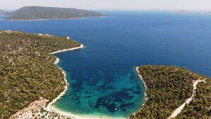 Vista aerea di una zona costiera con mare cristallino, spiaggia sabbiosa e strada che si snoda nel paesaggio.