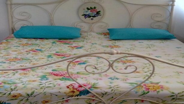 A bed with a floral bedspread, two blue pillows, and a decorative headboard with a floral design.