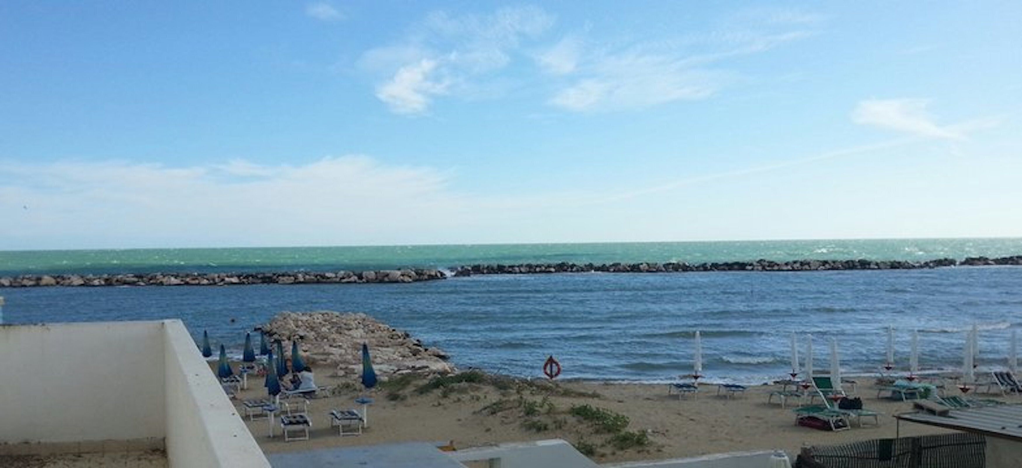 Une plage avec une digue rocheuse, des chaises longues et des parasols.