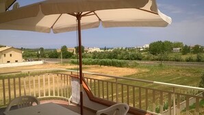 A balcony with a table and chairs, a large umbrella, and a view of a road and greenery. - Single Room for Rent With Private Bathroom (Montenero di Bisaccia)