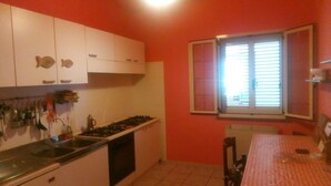A compact kitchen with white cabinets, a gas stove, and a window with blinds. - 6-bed Room for Rent With Private Bathroom - Molise (Montenero di Bisaccia)