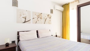 A bedroom with a bed, nightstands, wall art, an air conditioner, and a window with curtains. - Appartamento In Centro Siracusa (Syracuse)