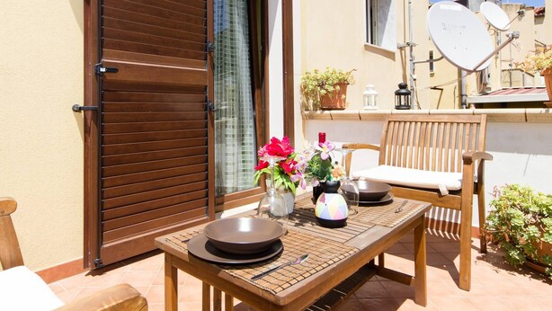 An outdoor patio with a wooden table set for dining, a wooden chair, and a sliding glass door. - Appartamento In Centro Siracusa (Syracuse)