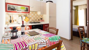 A compact kitchen with a dining area, featuring a table with a colorful tablecloth, a laptop, and a bottle of wine. - Appartamento In Centro Siracusa (Syracuse)