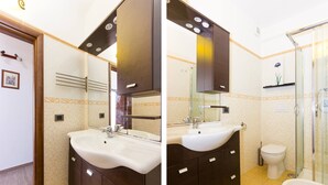 A bathroom with a double sink, dark wooden cabinets, a glass shower enclosure, and a toilet. - Appartamento In Centro Siracusa (Syracuse)
