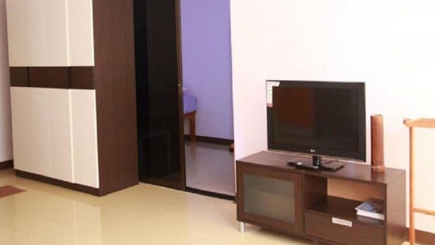 A room with a TV on a wooden stand, a wardrobe, and a door leading to another room. - Room-near Impact Challenger Bangkok Thai (Pak Kret)