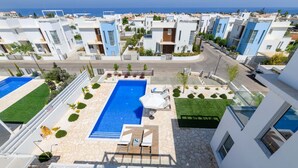 A modern residential area with a central swimming pool, surrounded by well-maintained lawns and a clear view of the sea.