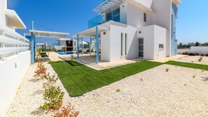 A modern, multi-story building with a white exterior and blue accents, featuring a covered outdoor area with seating and a pool.
