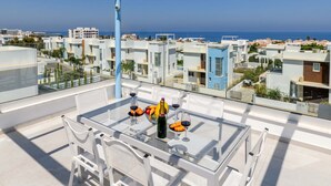 A rooftop terrace with a glass table, white chairs, and a bottle of wine.