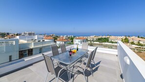 Eine Dachterrasse mit Glastisch, Stühlen und einer Champagnerflasche.