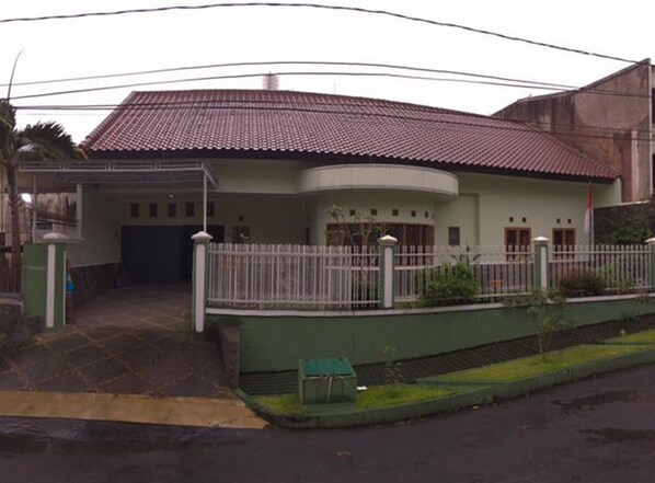 Una casa de dos pisos con techo curvo, un patio delantero cercado y un pequeño jardín verde.